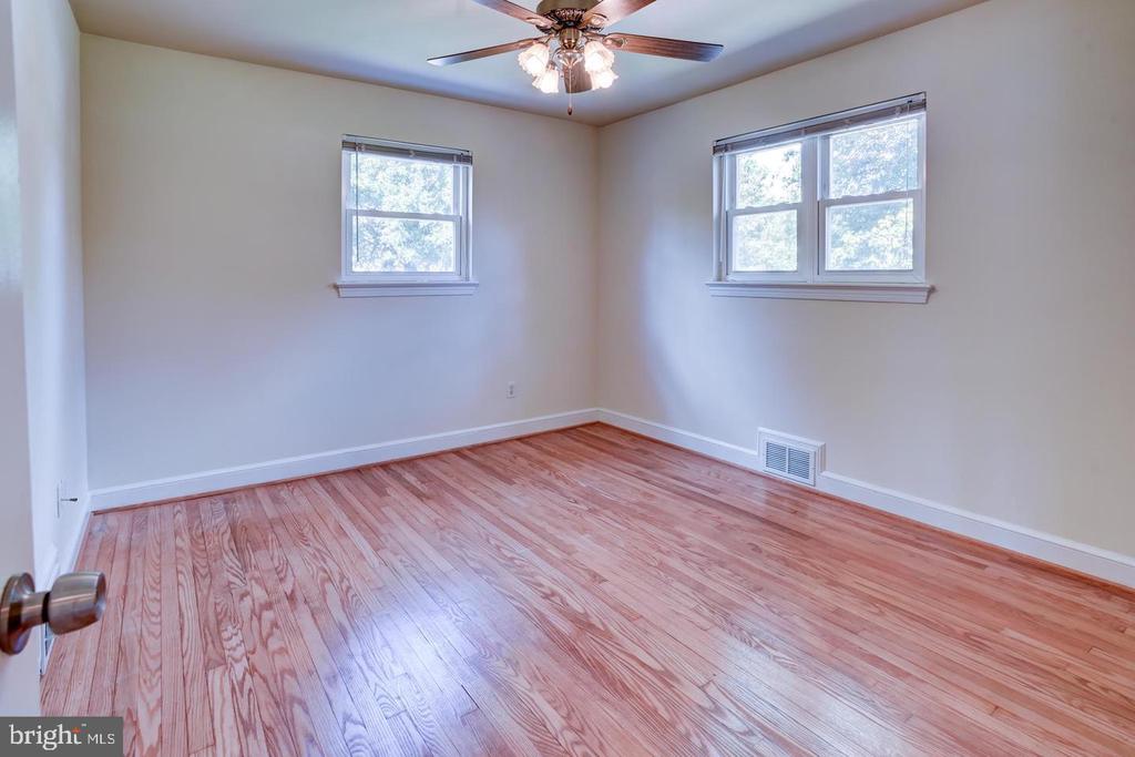Empty bedroom with polished hardwood floors, two windows, and a ceiling fan with light.