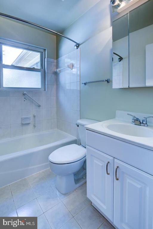 Bathroom with a tub-shower, toilet, and white vanity beneath a mirrored cabinet.