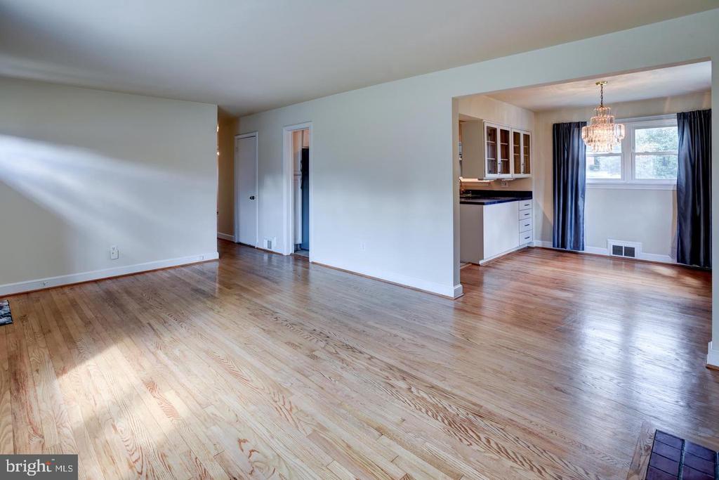 Unfurnished living and dining area with hardwood floors, open kitchen, and sunlight through windows.