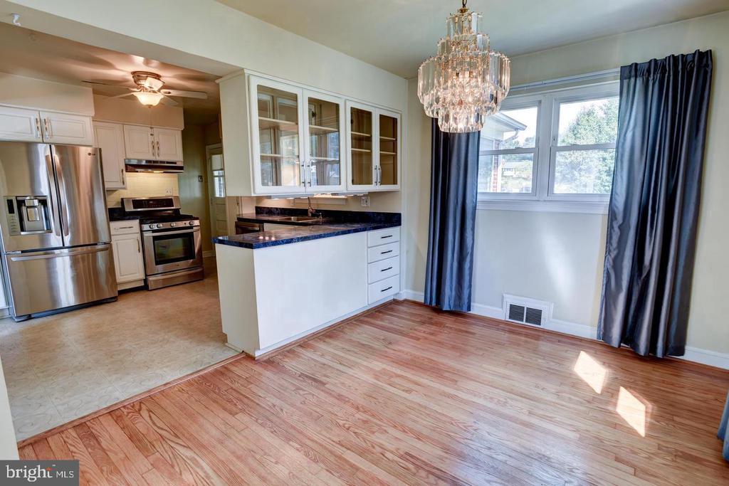 Kitchen and dining area with white cabinetry, stainless appliances, hardwood floors, and a crystal chandelier.