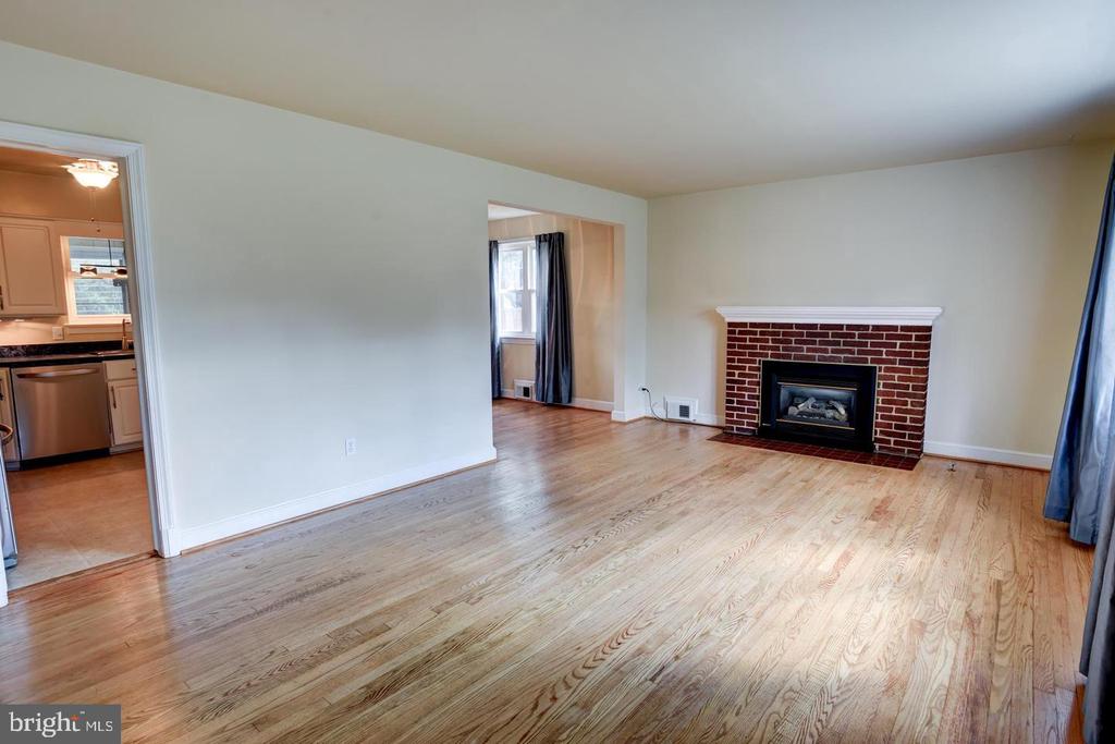 Empty living room with hardwood floors and a red-brick fireplace, viewed toward the kitchen doorway.