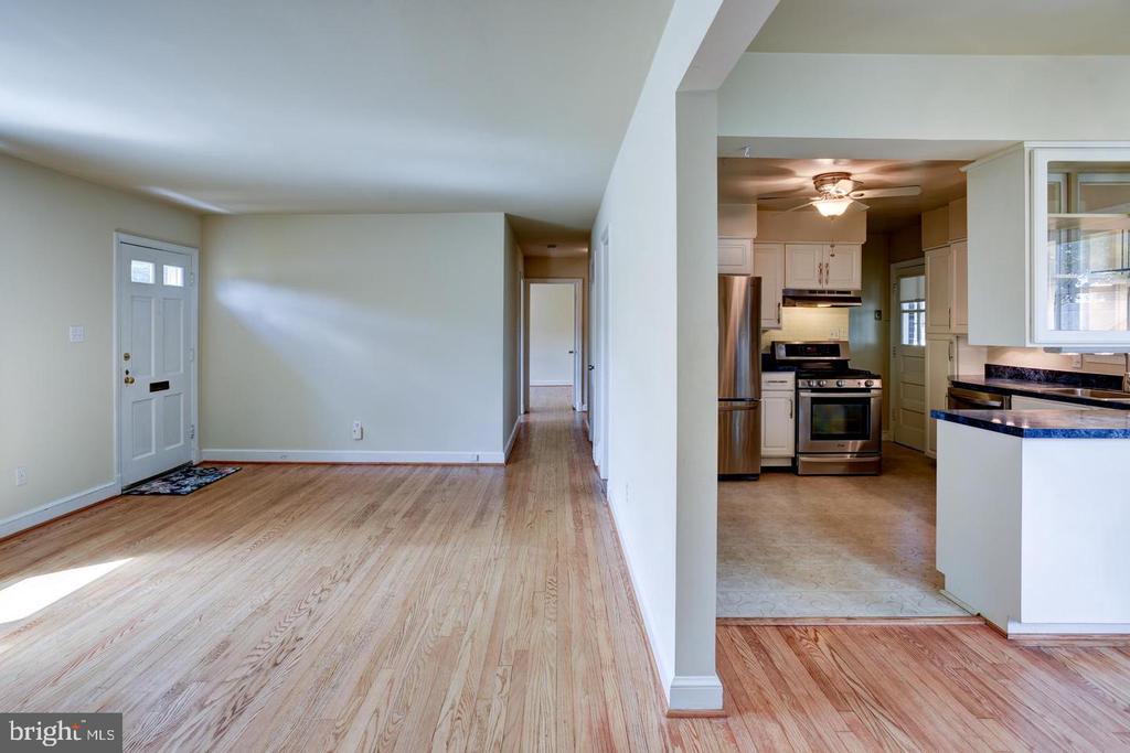 Empty living area with hardwood floors opens to a white kitchen with stainless steel appliances.