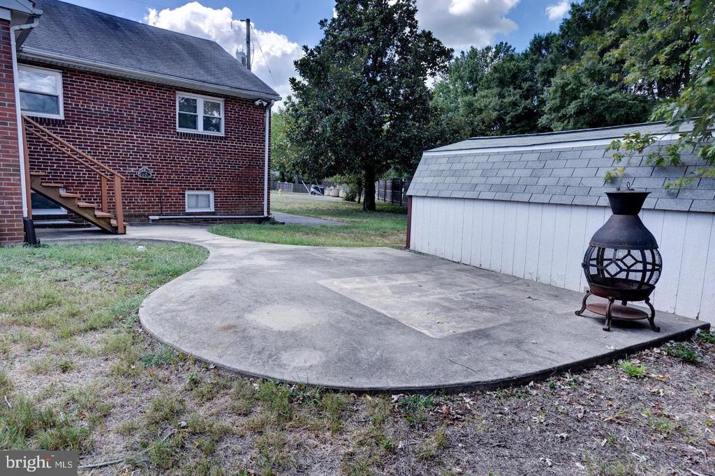 Brick house backyard with a concrete patio, white shed, and freestanding chiminea.