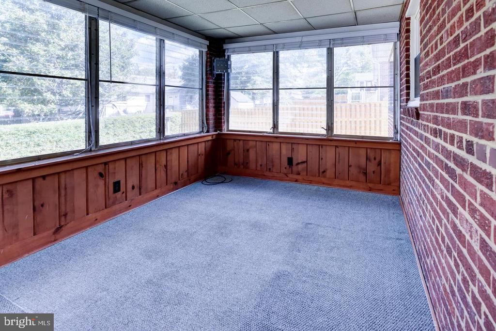 Empty sunroom with wraparound windows, gray carpet, wood paneling, and a brick wall.