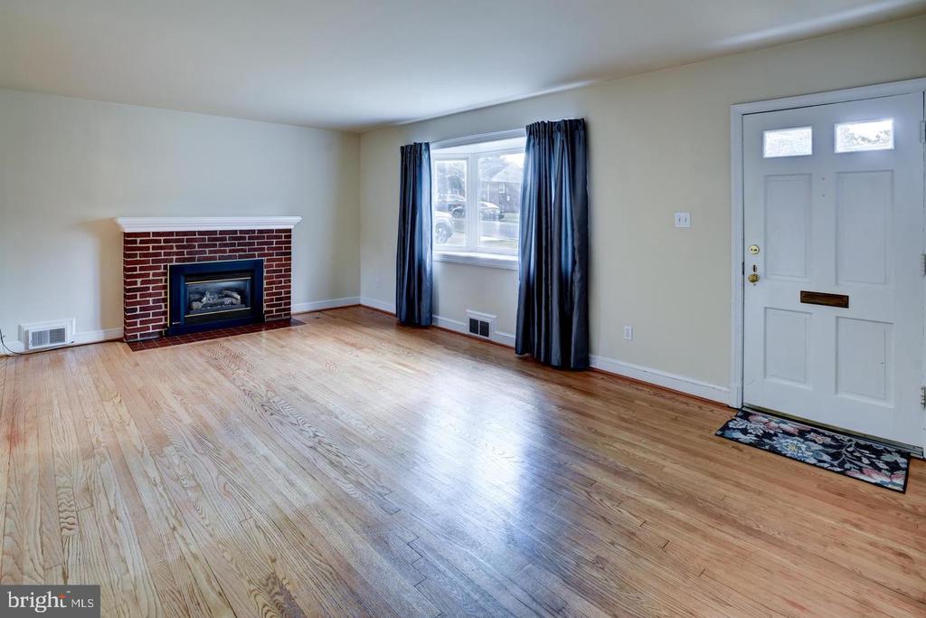 Living room with hardwood floors, a brick fireplace, and a curtained window.