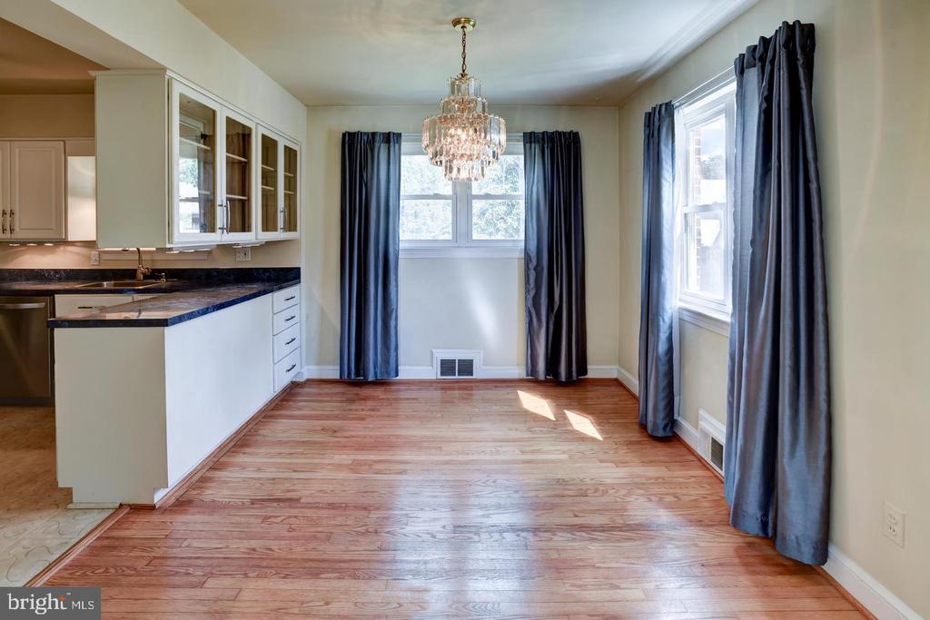 Dining area with hardwood floors, a crystal chandelier, and dark curtains beside the kitchen.