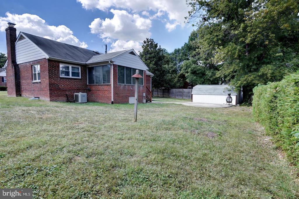 Rear of a red-brick house across a broad lawn, with a detached white shed and mature trees.