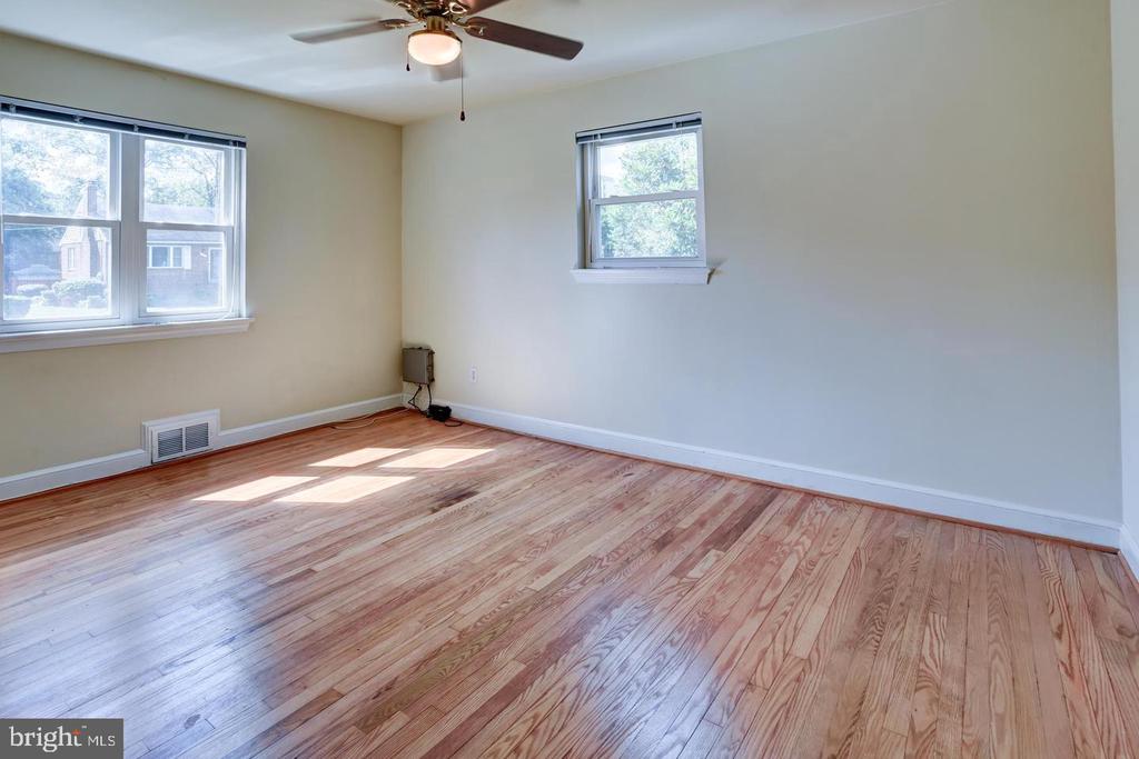 Empty room with polished hardwood floors, two windows, and a ceiling fan.