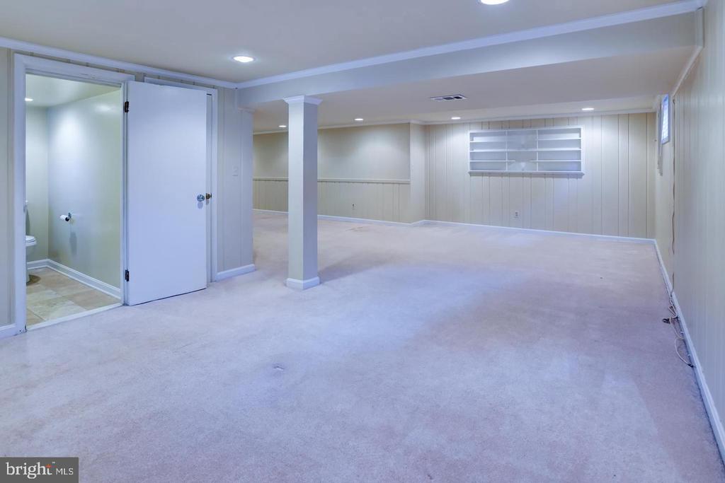 Finished basement rec room with carpet, paneled walls, built-in shelves, and an adjoining bathroom.