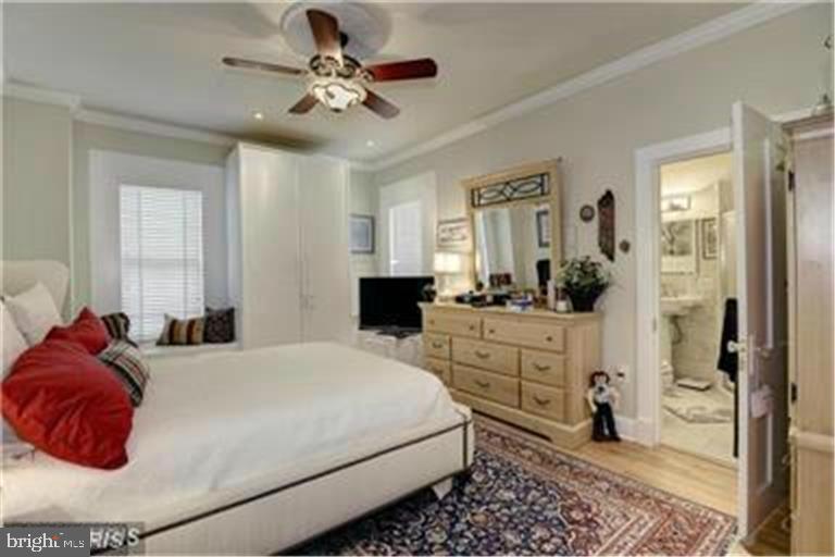 Bedroom with a white bed, red pillows, wooden dresser, and patterned rug.