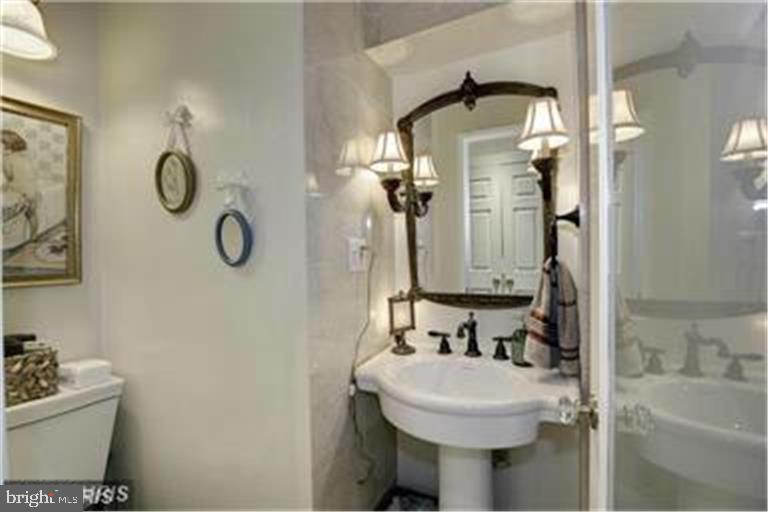 Traditional bathroom with a pedestal sink, ornate mirror, and glass-enclosed bathtub.