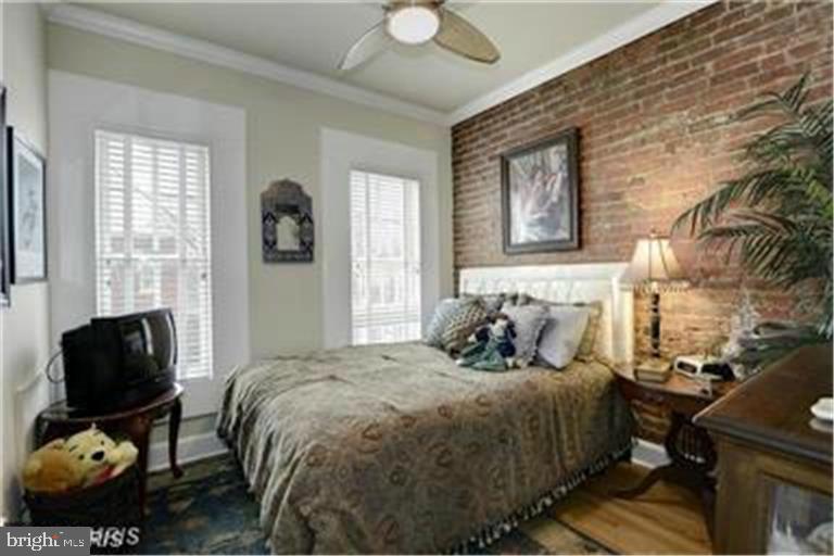 Bedroom with an exposed brick accent wall, shuttered windows, and a large bed.