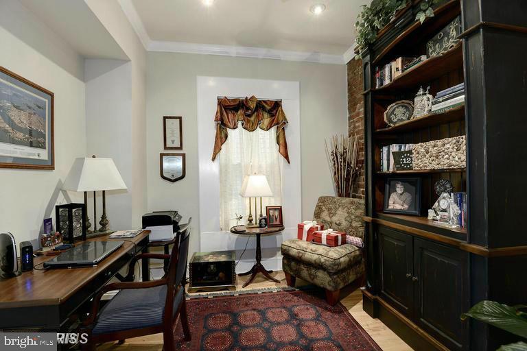 Furnished study with a tall built-in bookcase, wooden desk, and patterned rug.