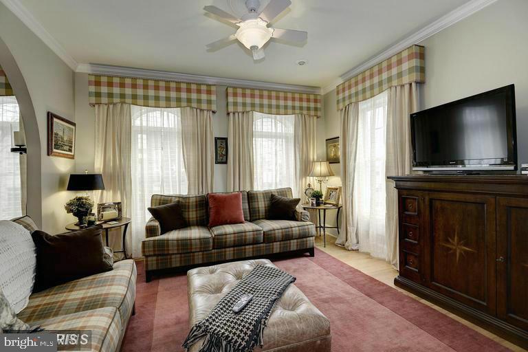 Living room with plaid sofas, tall curtained windows, and a television on a dark wood cabinet.