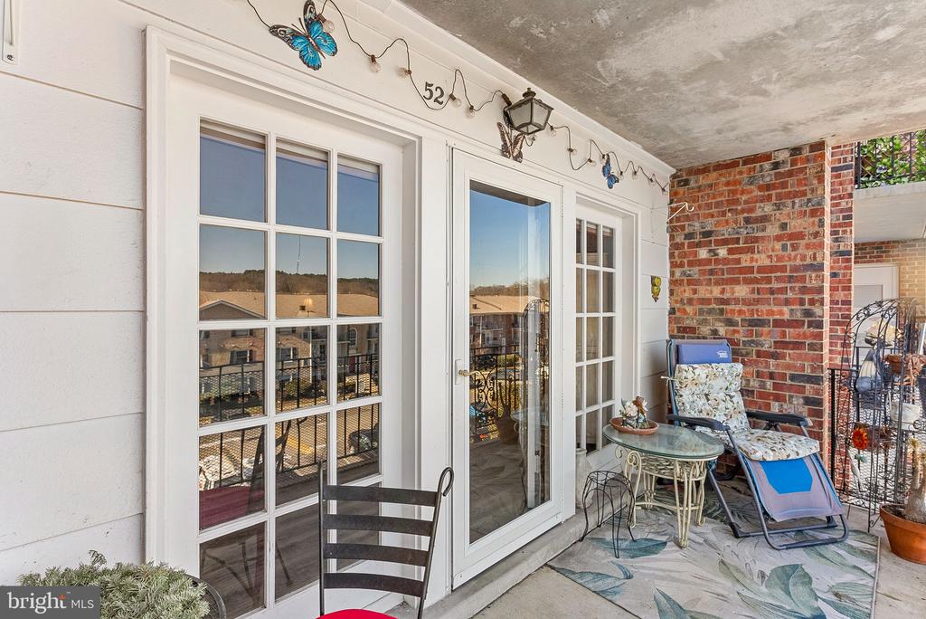 Covered patio with a glass sliding door, brick wall, and outdoor seating.