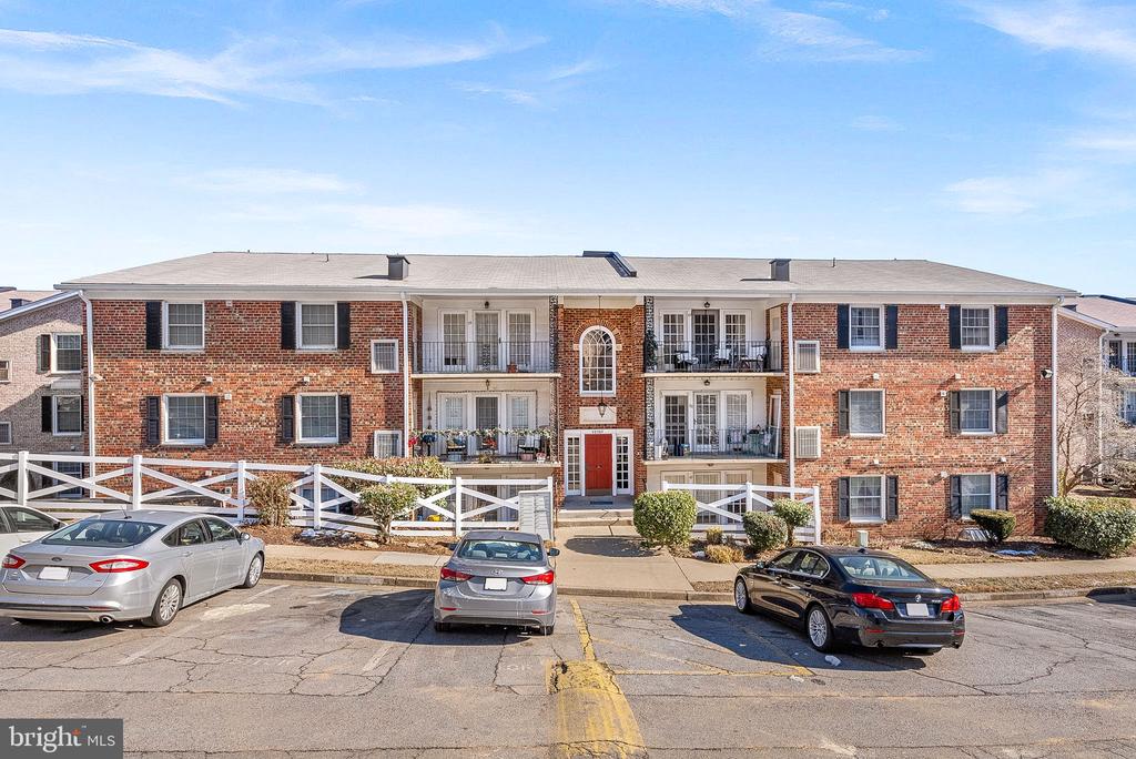 Red-brick condominium building with balconies and parked cars in front.
