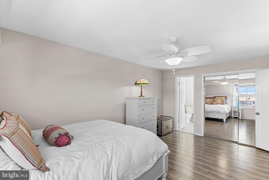 Furnished bedroom with a white bed, patterned pillows, and mirrored closet doors reflecting another bedroom.