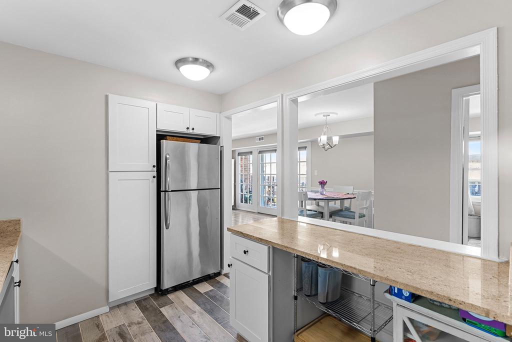 Kitchen with white cabinets, stainless steel refrigerator, and a stone counter overlooking the dining room.