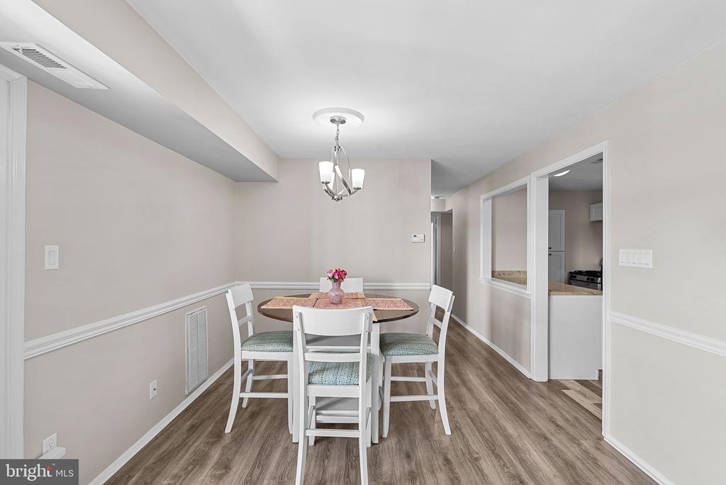 Dining room with a round table, white chairs, wood-look flooring, and a chandelier.