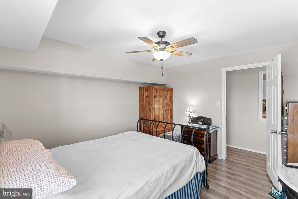 Bedroom with a large bed, rustic wooden wardrobe, ceiling fan, and open doorway.