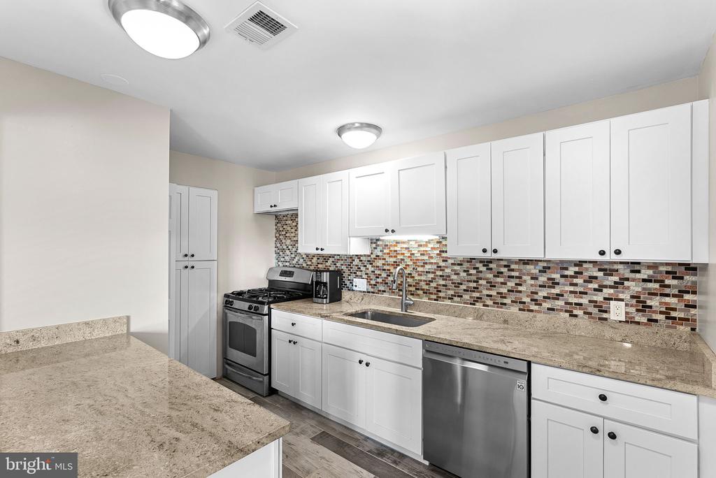 Kitchen with white cabinets, granite counters, mosaic tile backsplash, and stainless steel appliances.