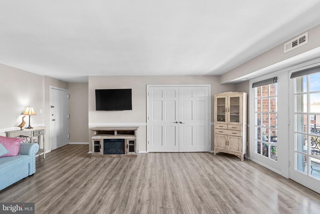 Living room with a fireplace, wall-mounted TV, gray flooring, and French doors to a balcony.