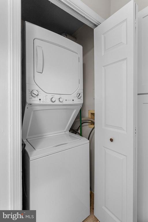 Stacked washer and dryer in a narrow closet with the door open.