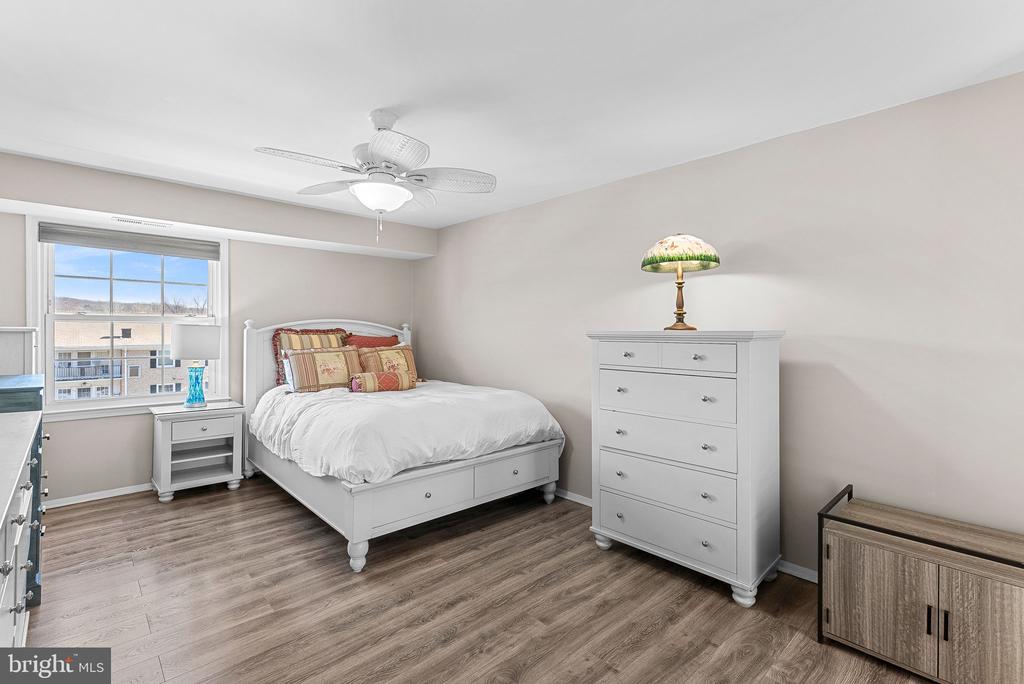 Bedroom with a white bed, matching furniture, ceiling fan, and wood-look flooring.