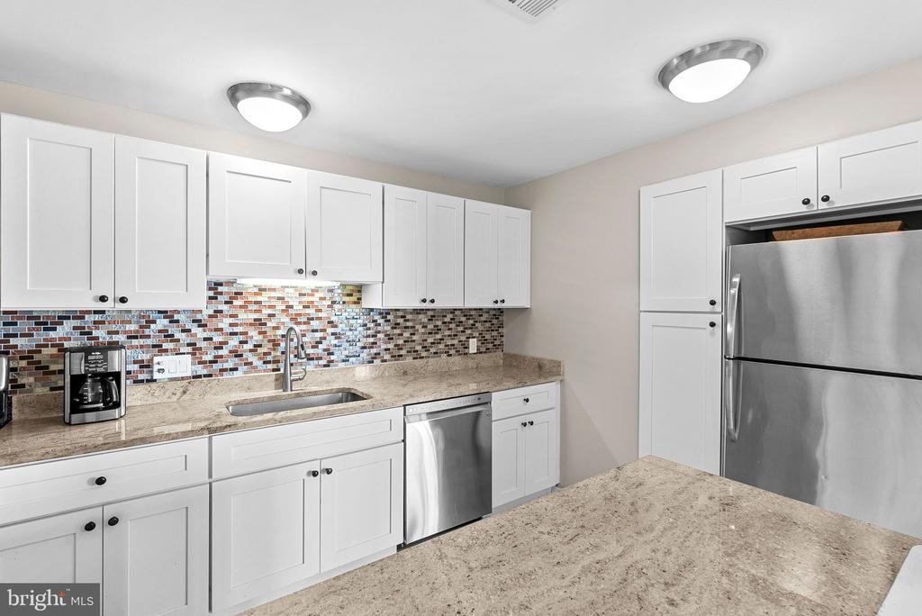Kitchen with white cabinets, granite counters, mosaic backsplash, and stainless steel appliances.