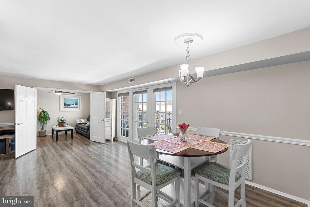 Dining room with a round table and chairs beside tall windows, opening to a living area.