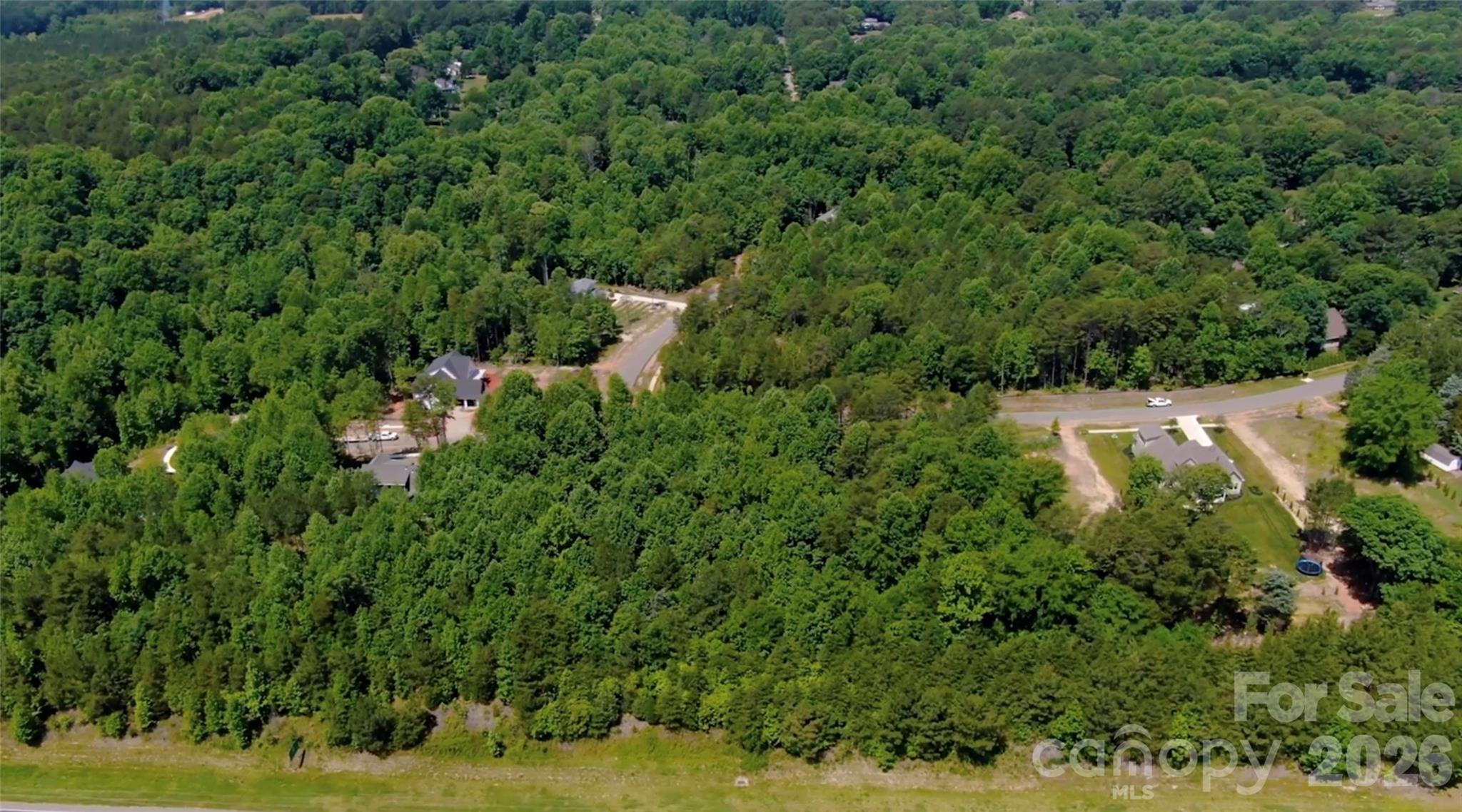 Aerial view of wooded homesites and a curving neighborhood road.