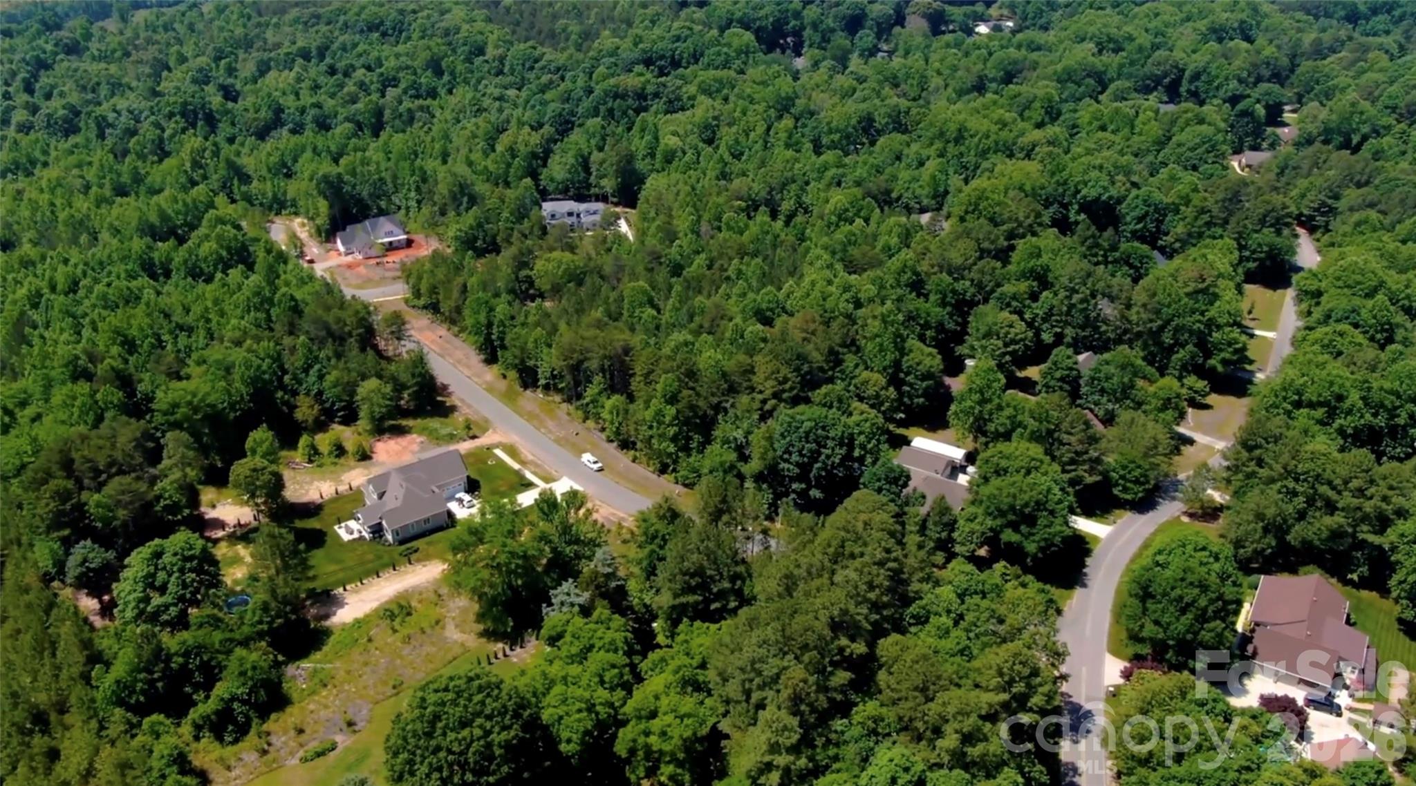 Aerial view of homes and roads among dense green trees, with cleared construction lots.