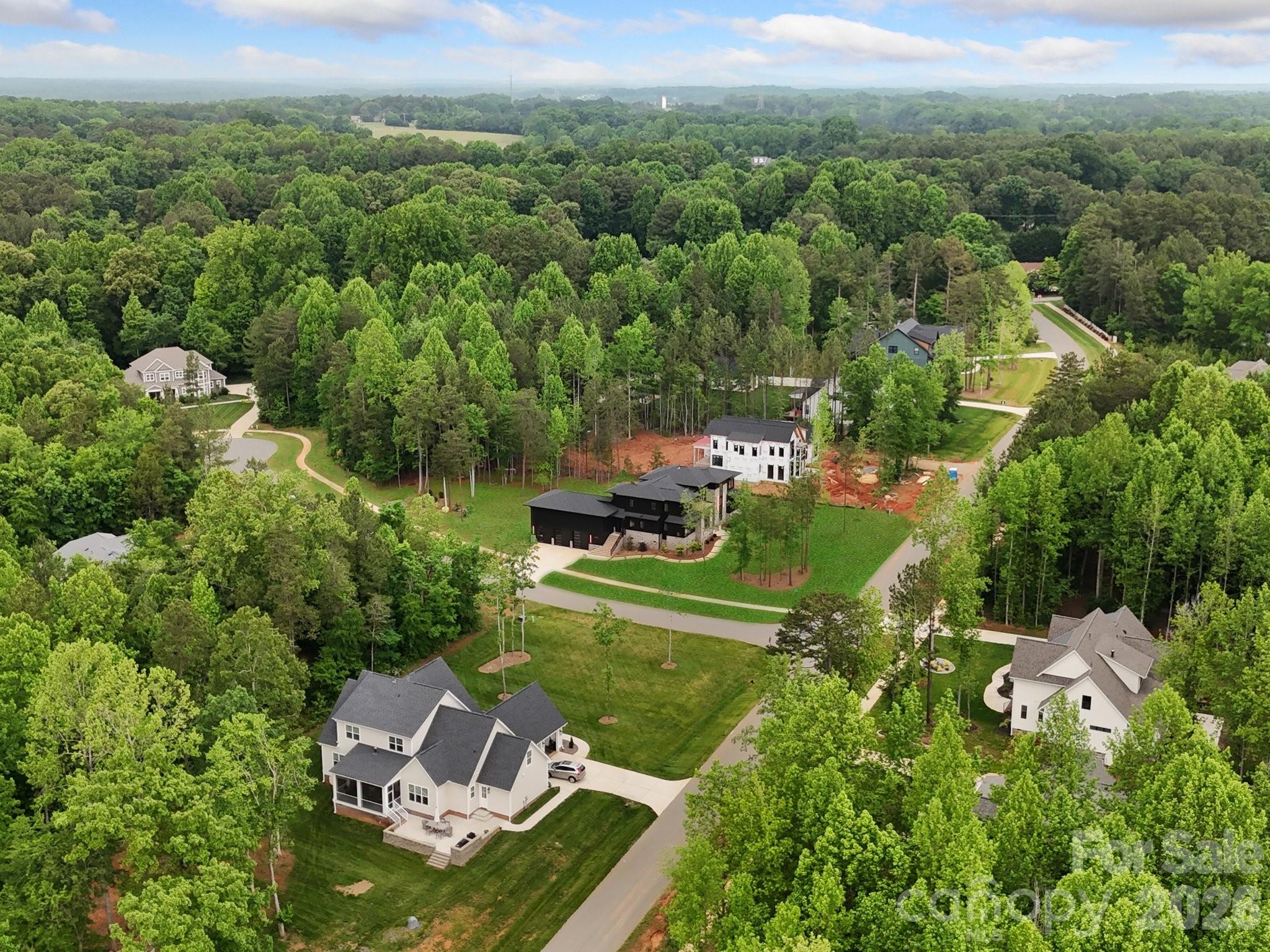 Aerial view of wooded neighborhood with curving roads and homes, including a new house under construction.
