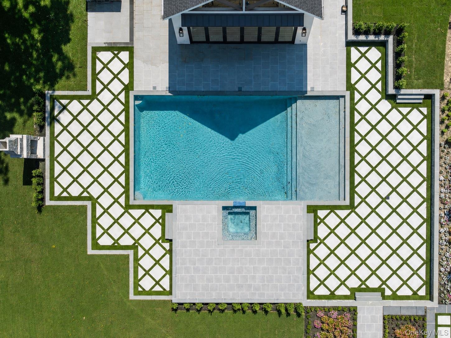 Aerial view of a rectangular backyard pool with an attached spa and geometric stone-and-grass paving.