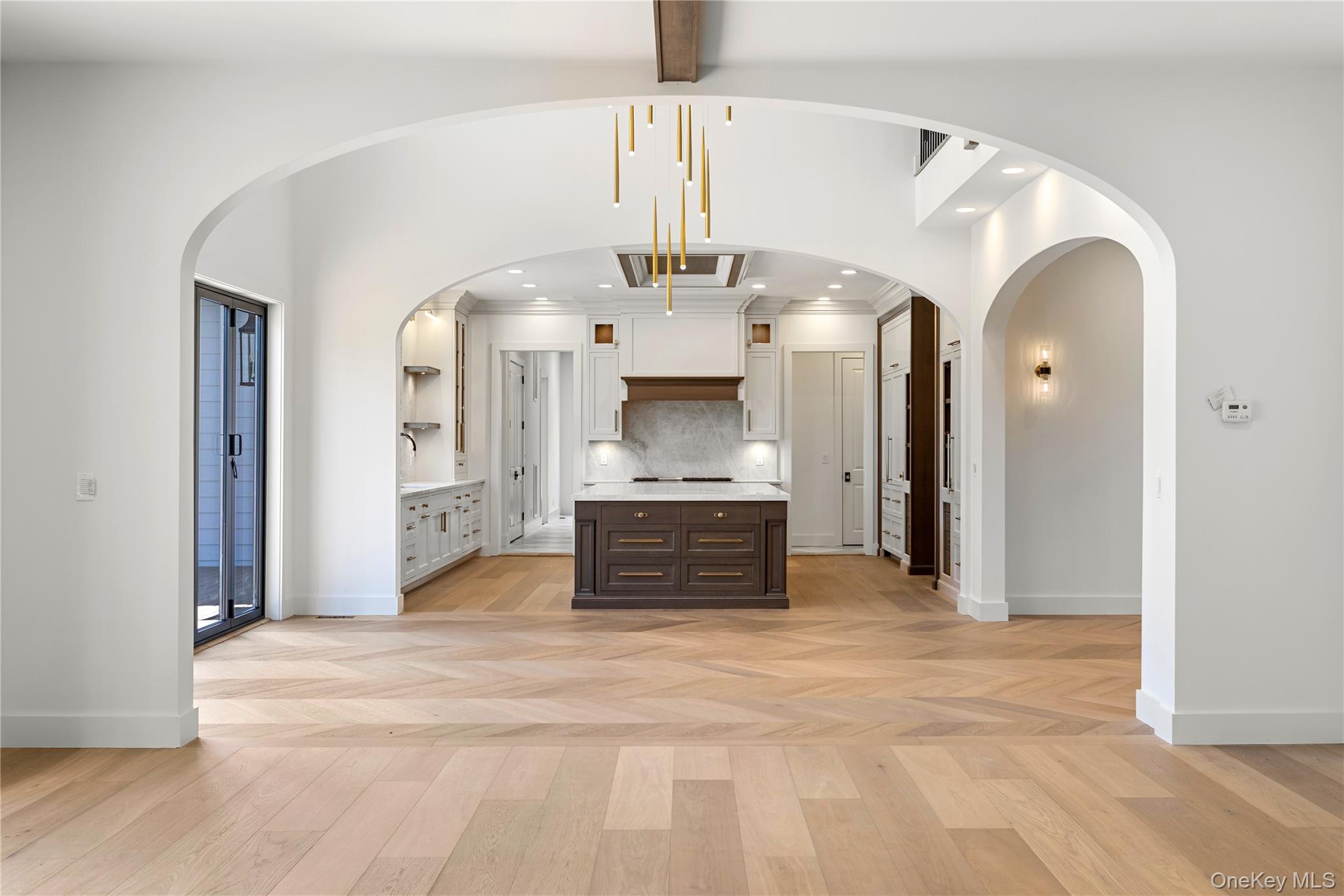 Bright kitchen with arched openings, a dark wood island, and pale herringbone oak flooring.