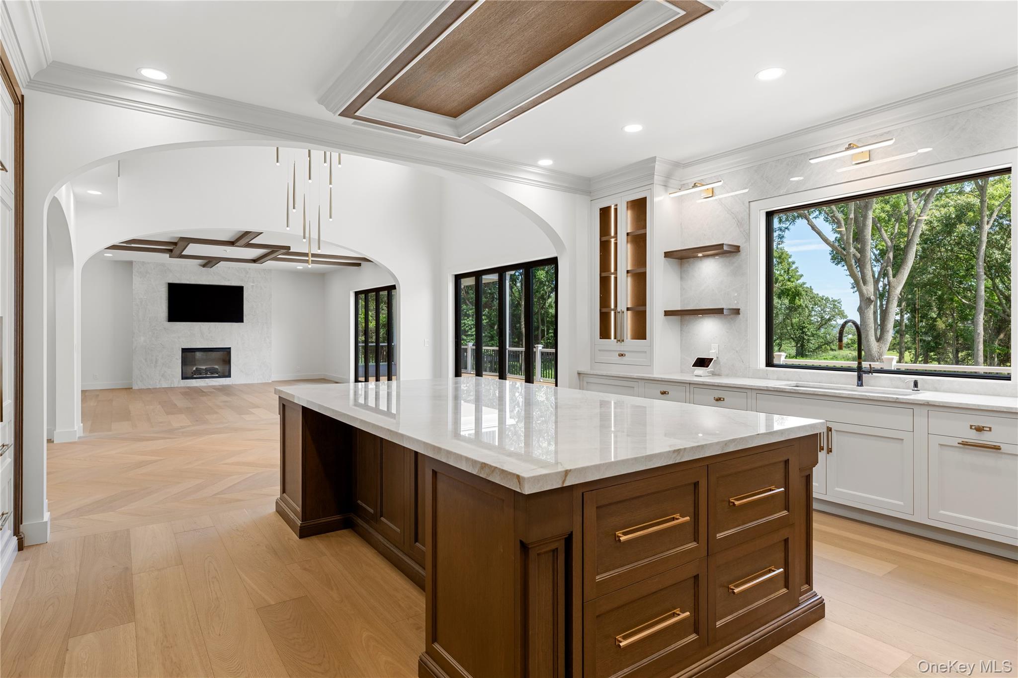Bright kitchen with a large dark wood island, white stone counters, and a wide window facing trees.