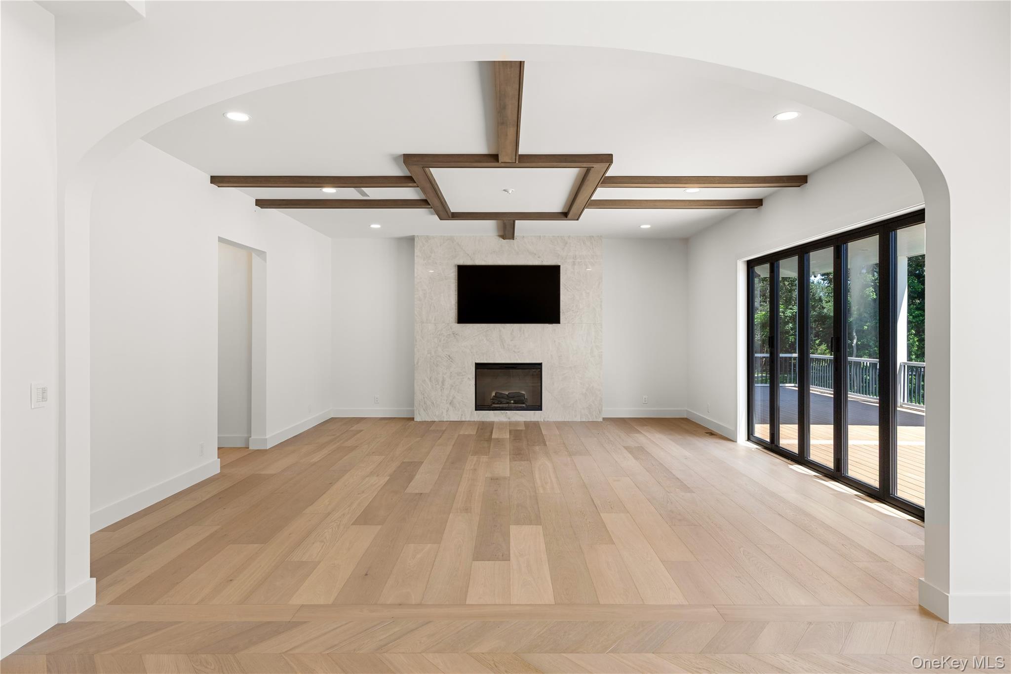 Vacant living room with wood floors, a marble fireplace wall, ceiling beams, and sliding doors to a deck.