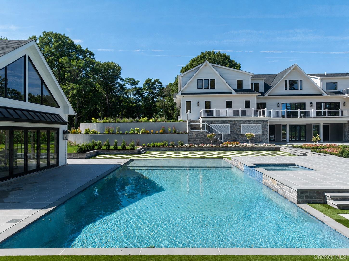 Large white house behind a swimming pool and landscaped patio.
