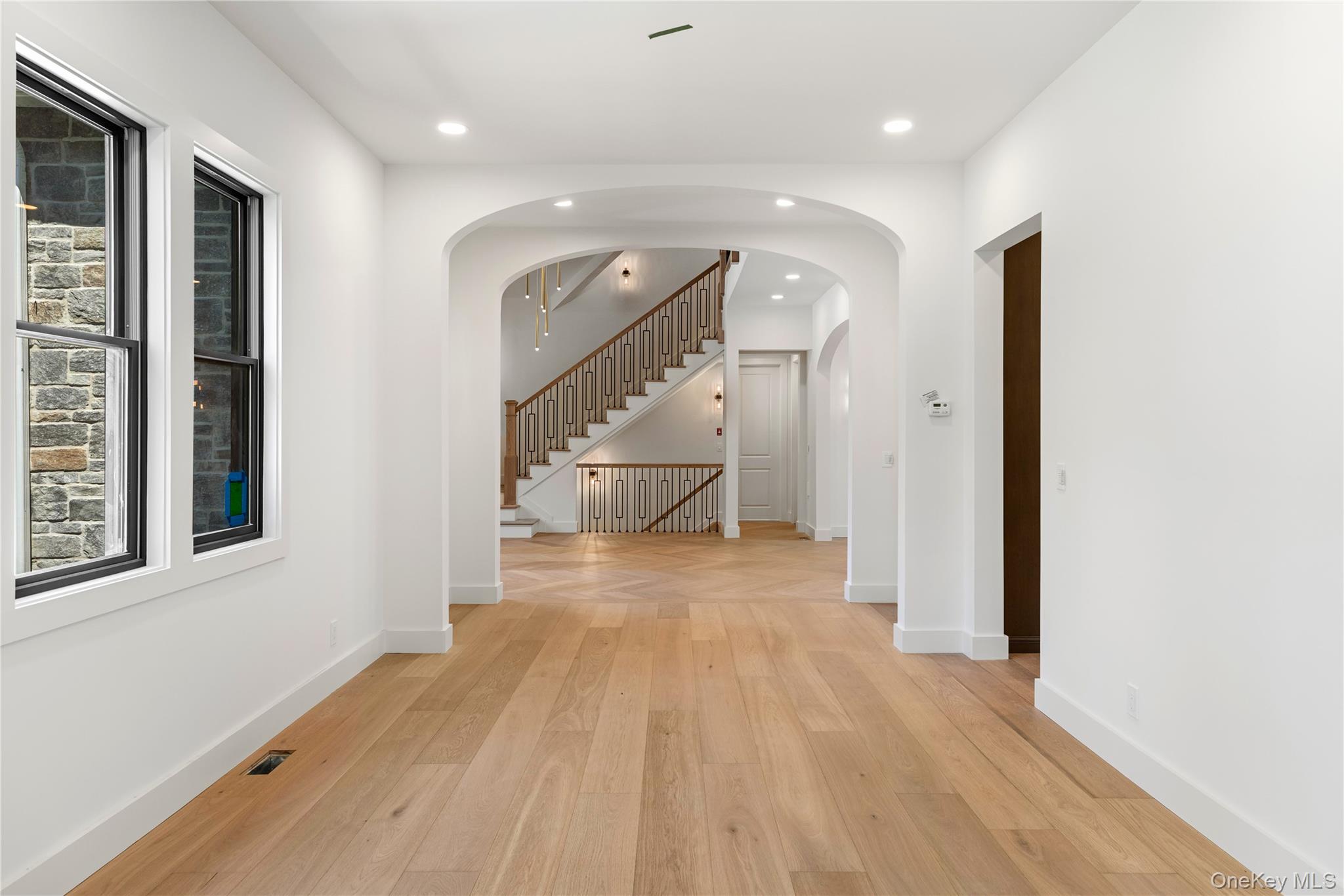 Unfurnished foyer with arched openings, light hardwood floors, and a staircase with dark metal balusters.