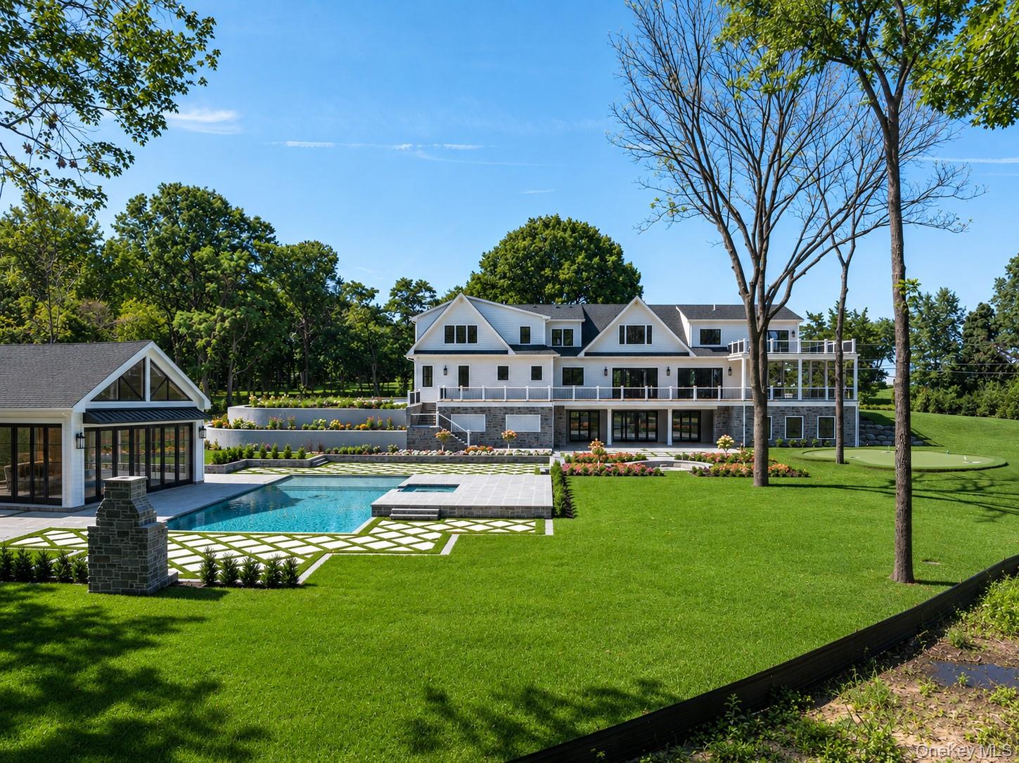 Large white-and-gray house with a swimming pool, pool house, and manicured lawn.