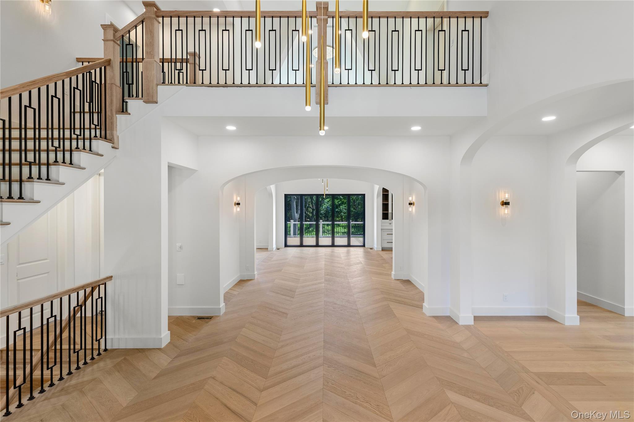 Two-story foyer with geometric stair railings, arched openings, and herringbone wood floors.