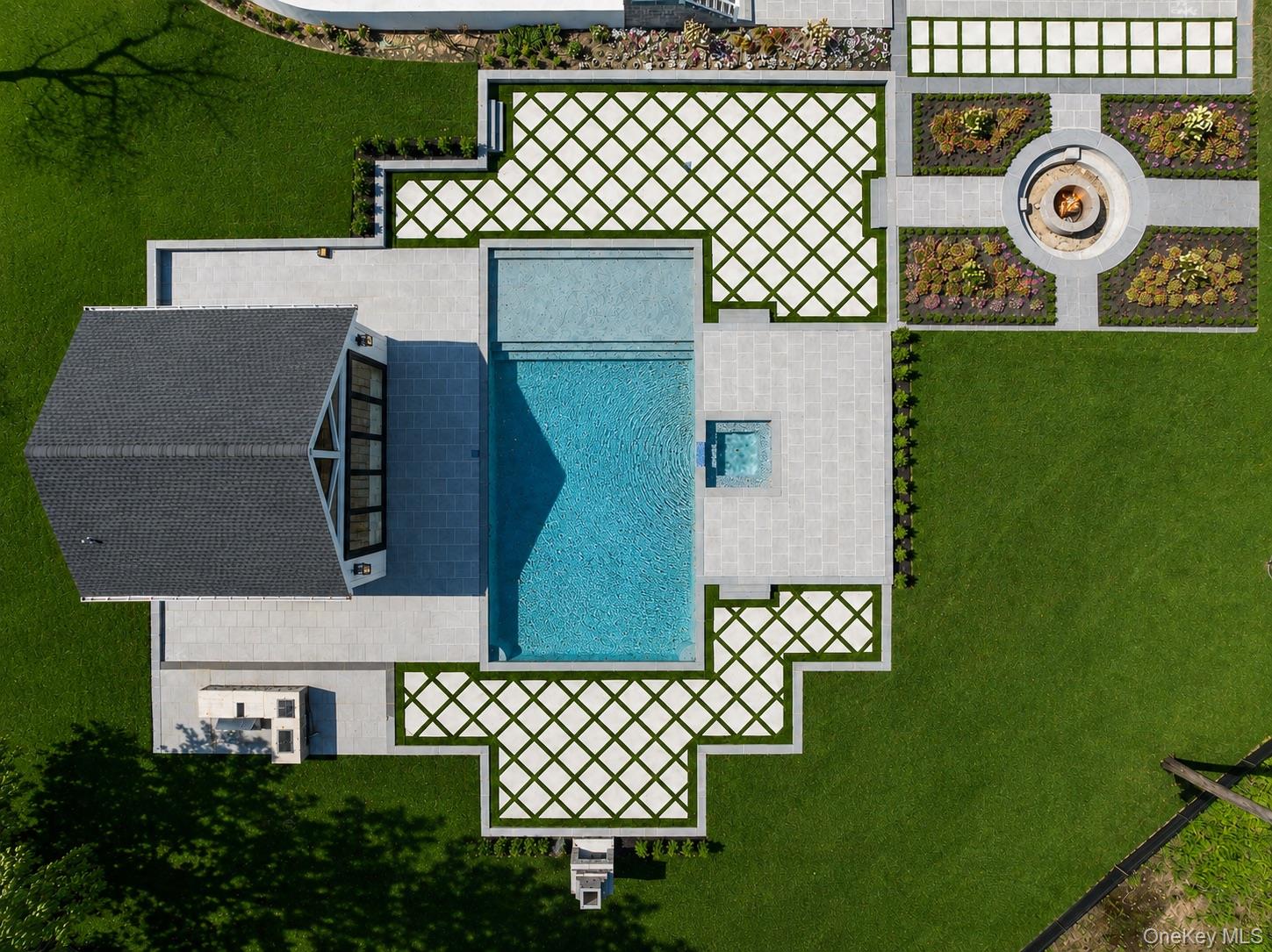 Aerial view of a backyard pool and spa, with geometric paving and a circular fire pit area.