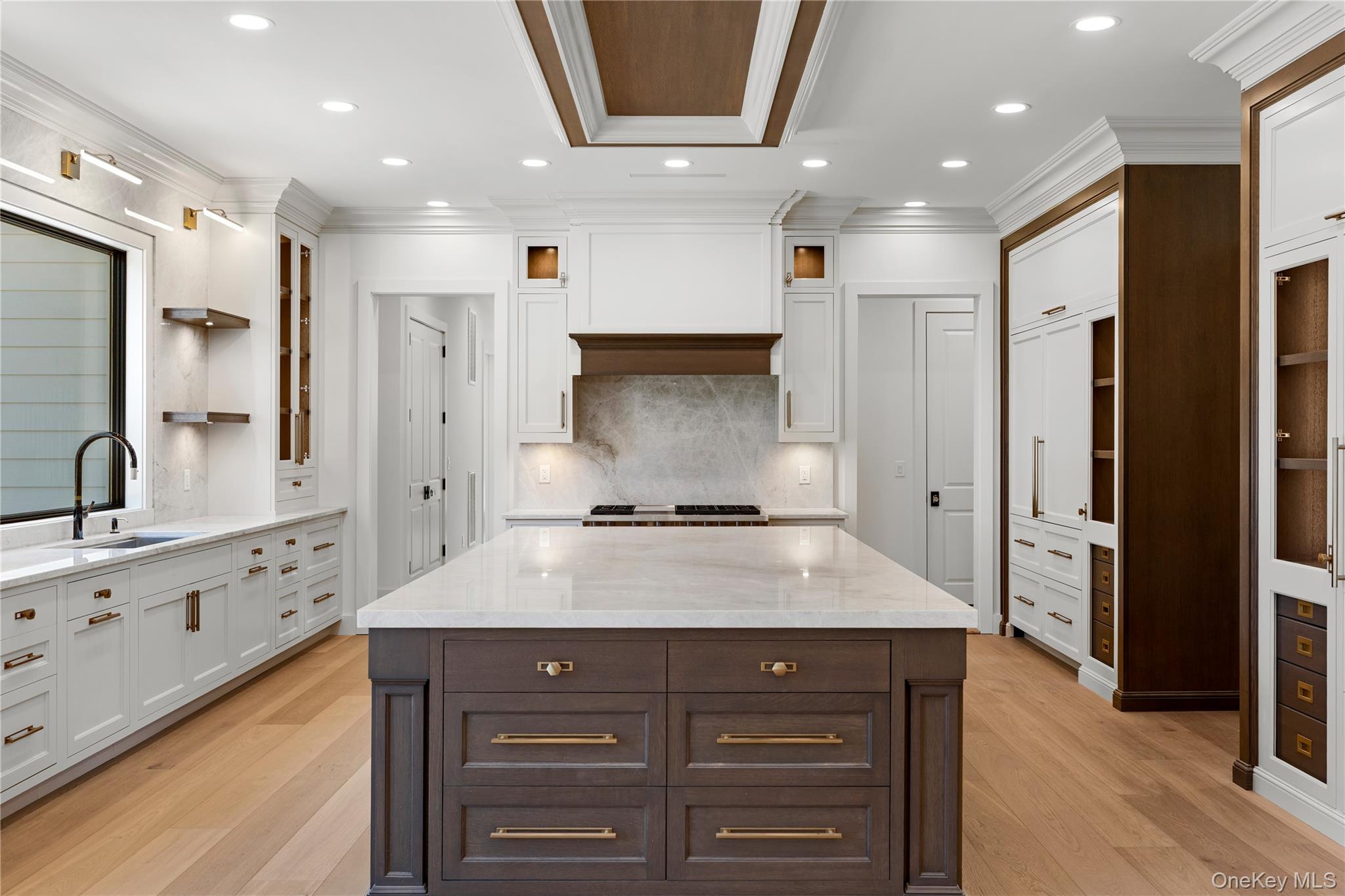 Kitchen with a large dark wood island, white stone counters, white cabinetry, and warm wood flooring.
