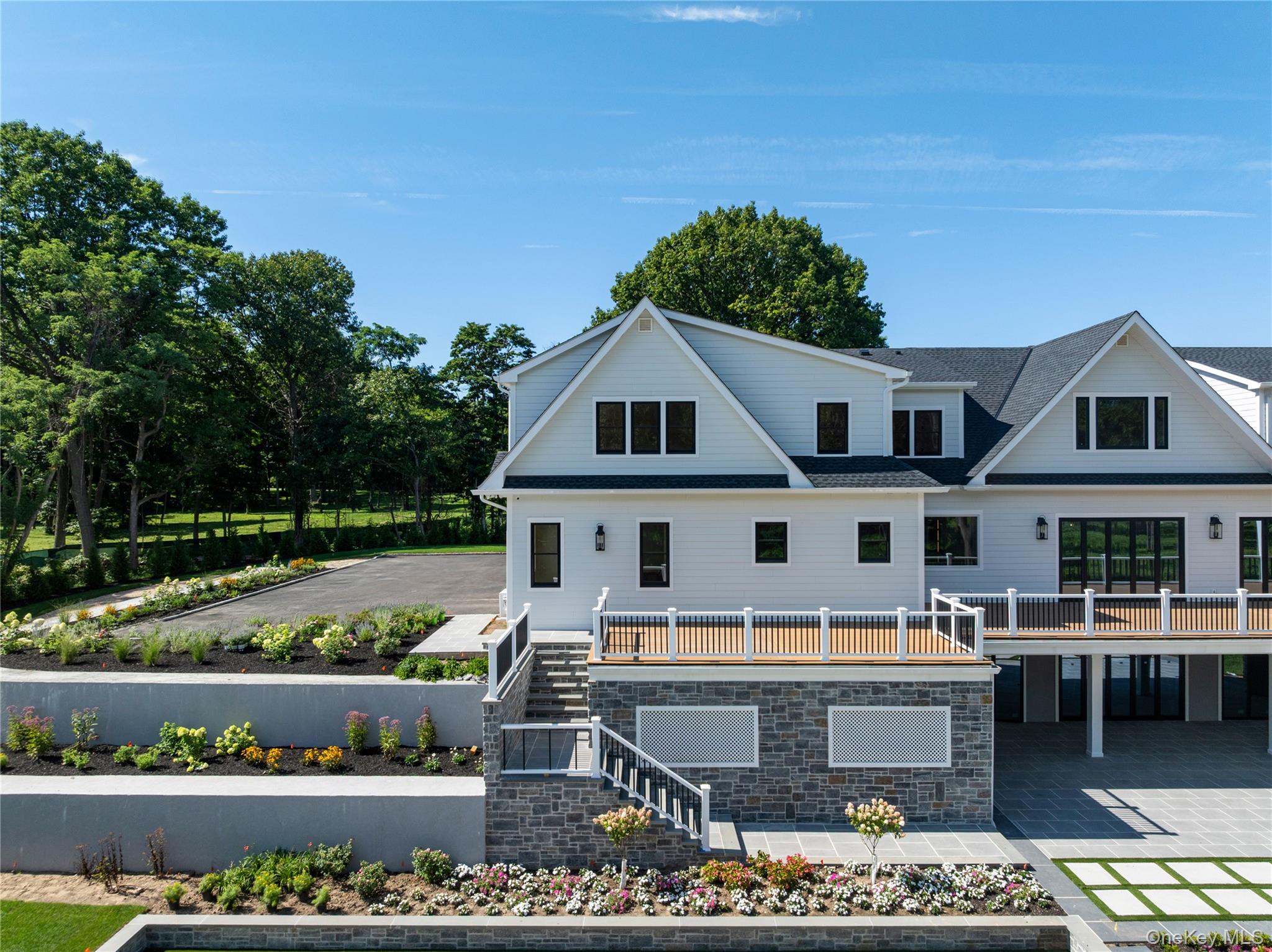 White multi-story home with stone lower level, elevated decks, and landscaped gardens.