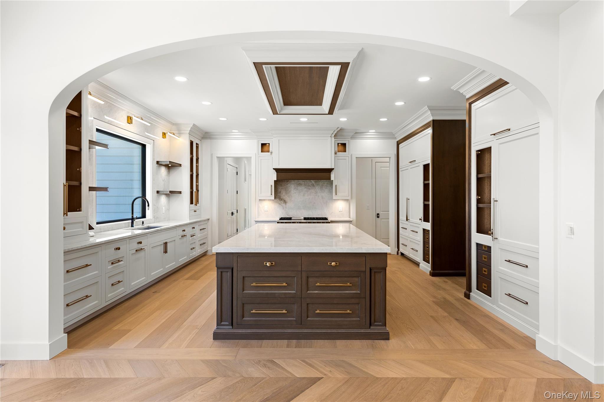Custom kitchen with a large marble island, white cabinetry, dark wood accents, and hardwood floors.
