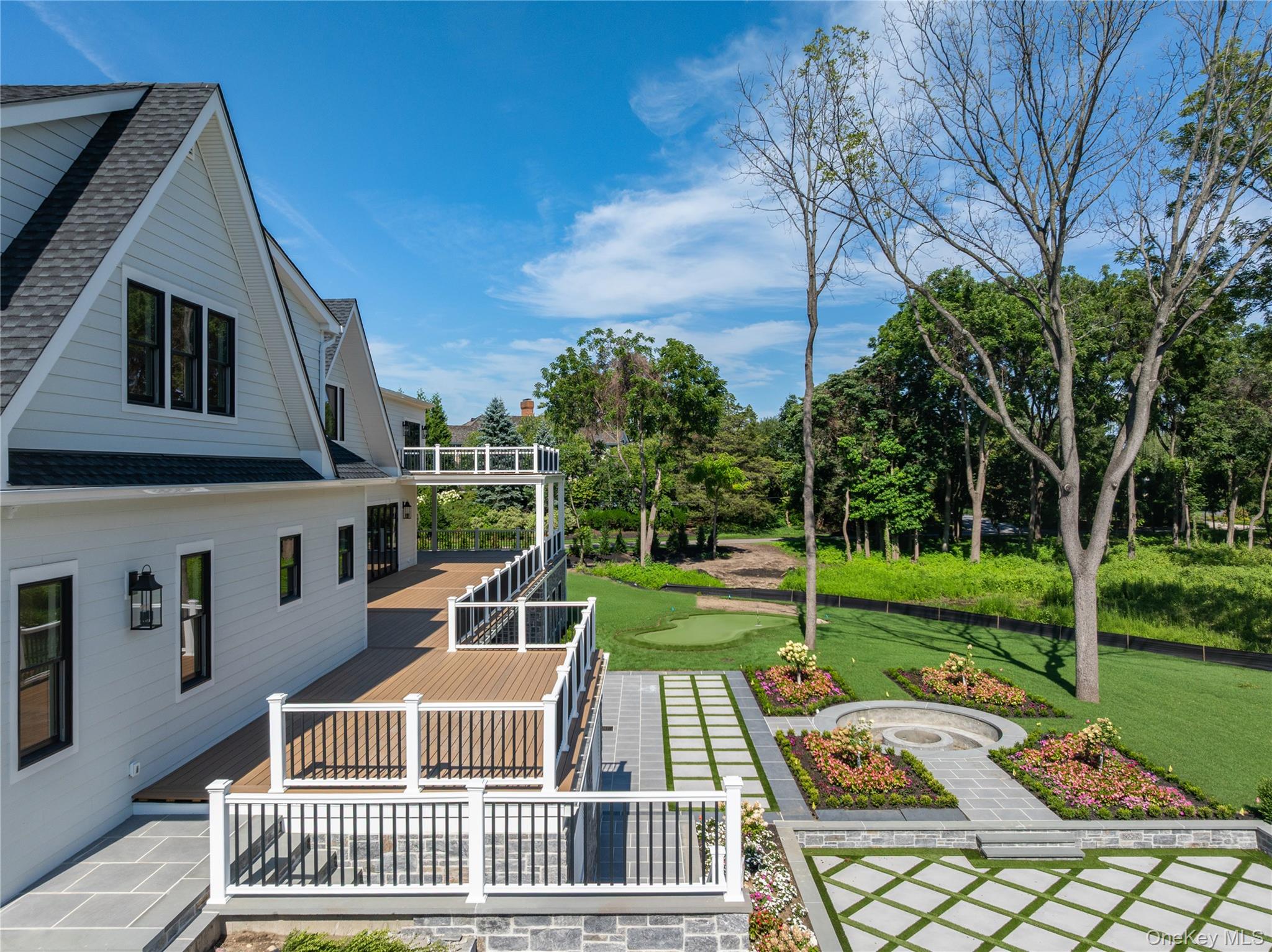 White-sided house with a multilevel deck beside a landscaped patio and circular fire pit.