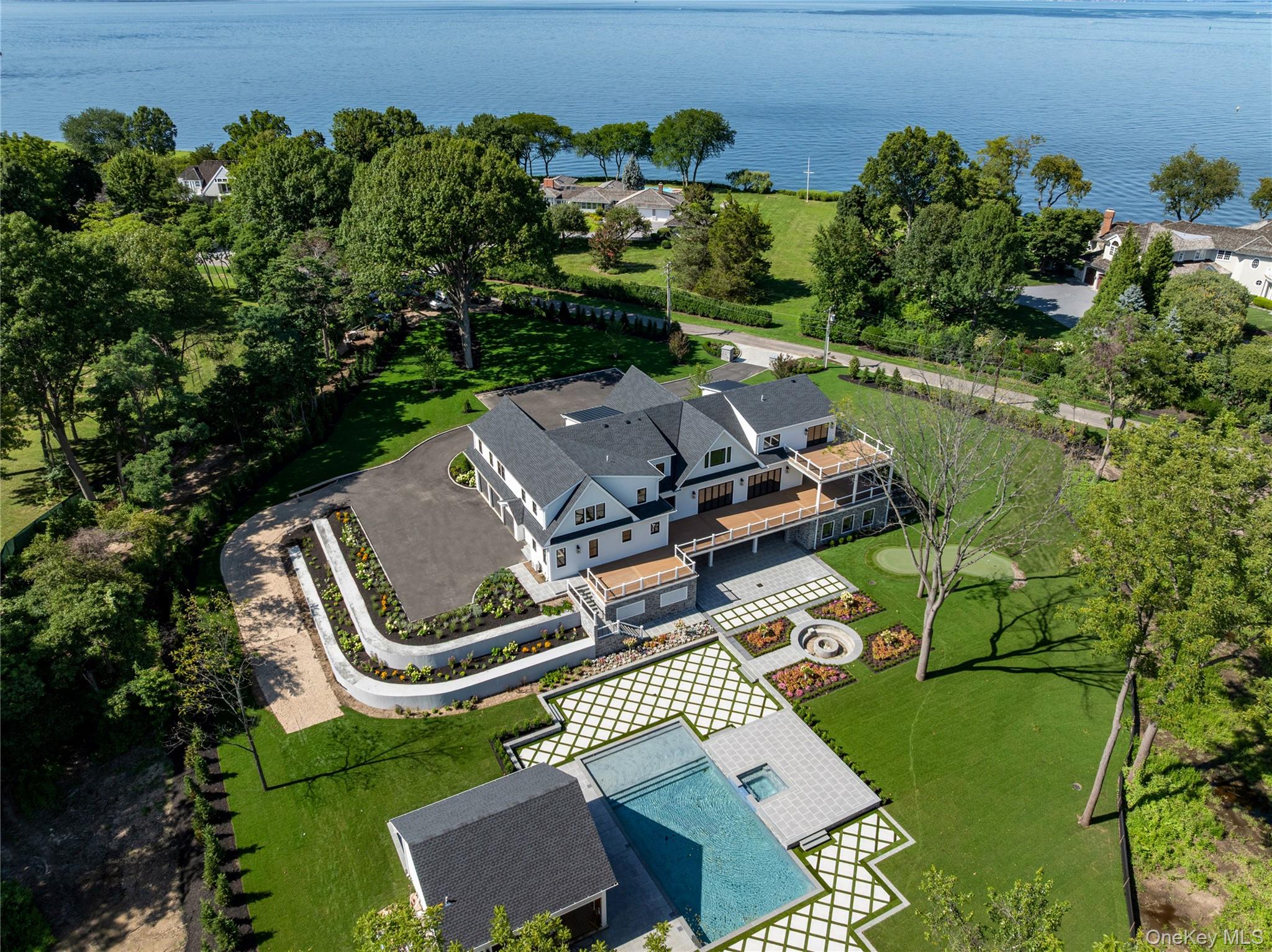 Waterfront home with expansive decks, landscaped grounds, and a long swimming pool beside the water.