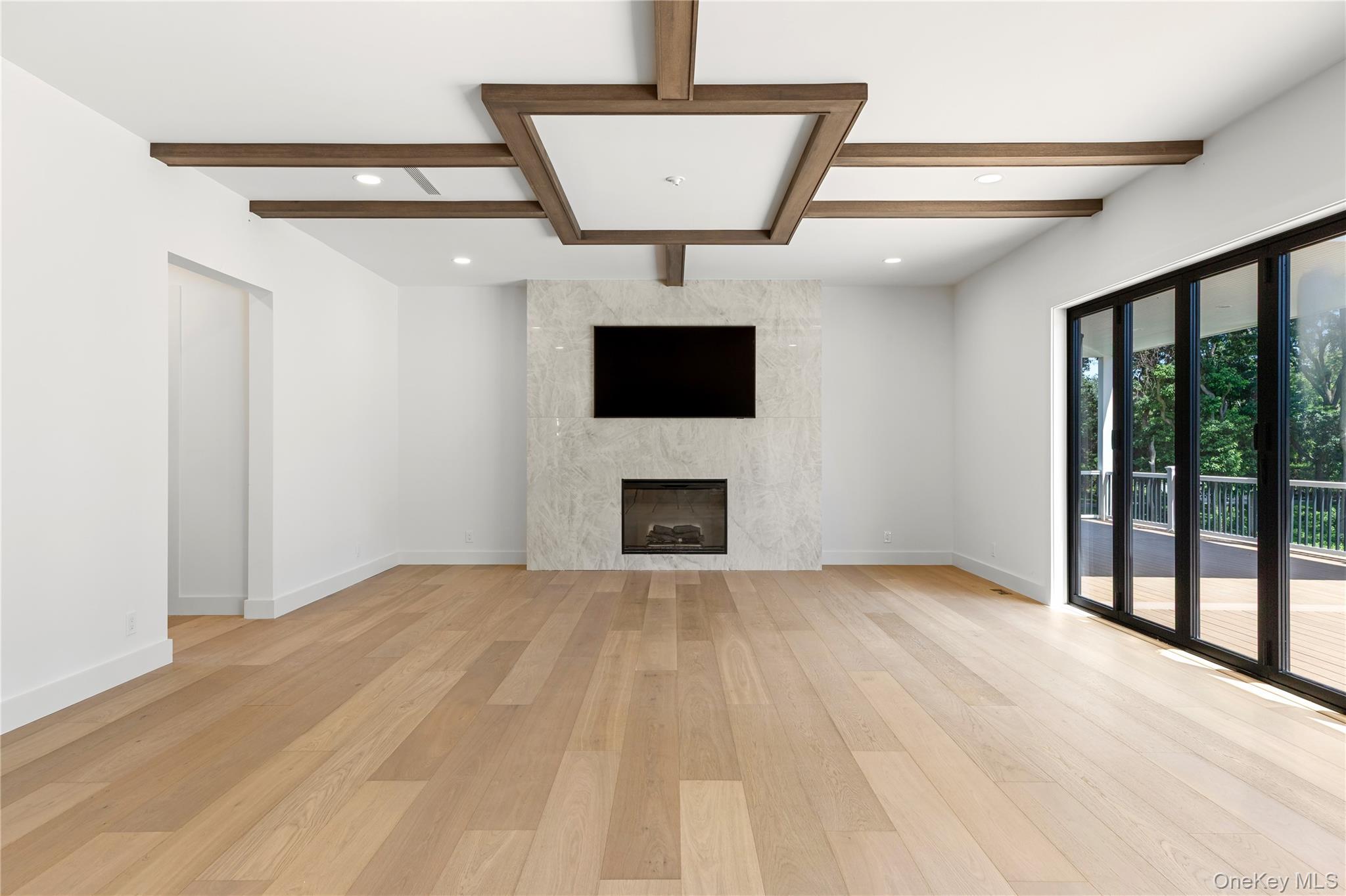 Vacant living room with wood floors, a marble fireplace wall, and sliding glass doors to a deck.