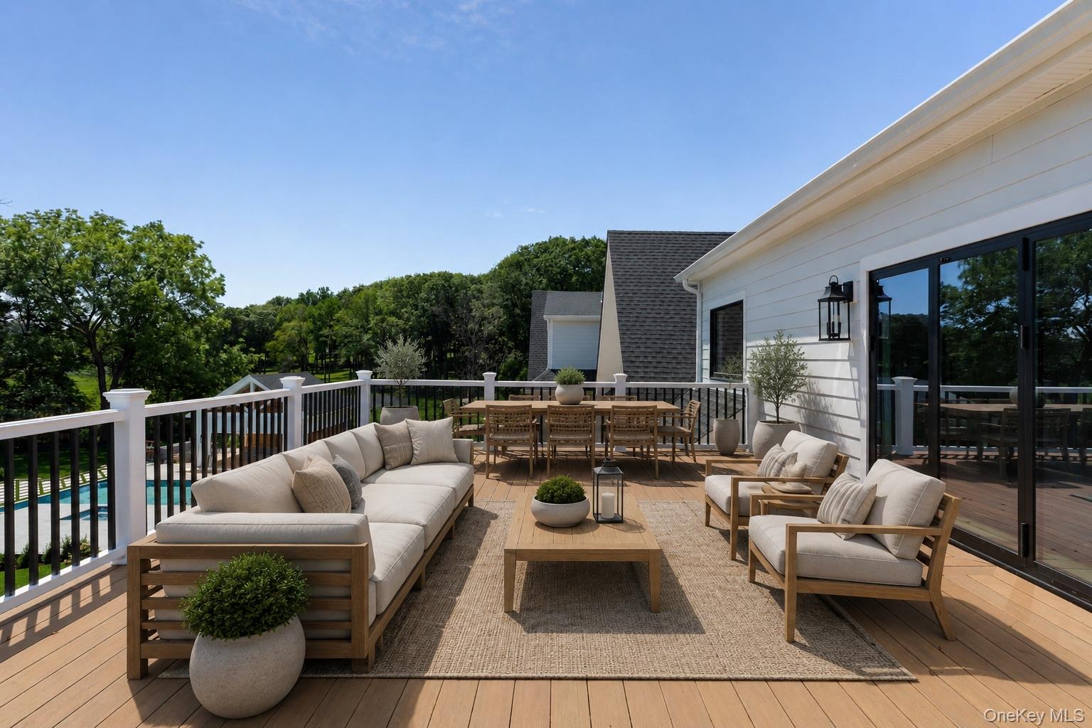 Furnished wooden deck with lounge seating, an outdoor dining table, and a pool visible below.