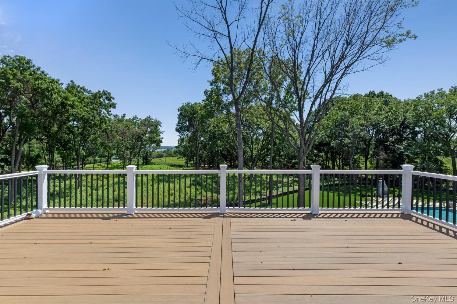 Wood deck overlooking wooded grounds and a glimpse of water, with part of a pool visible at right.